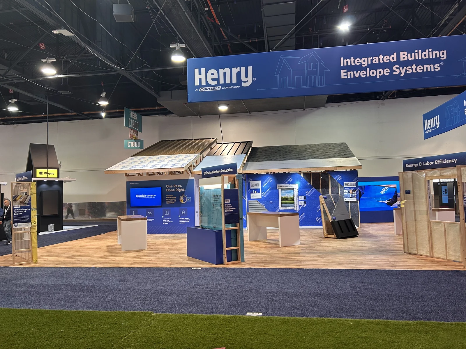 The booth on the show floor: framed walls, open rafters, the Henry sign above